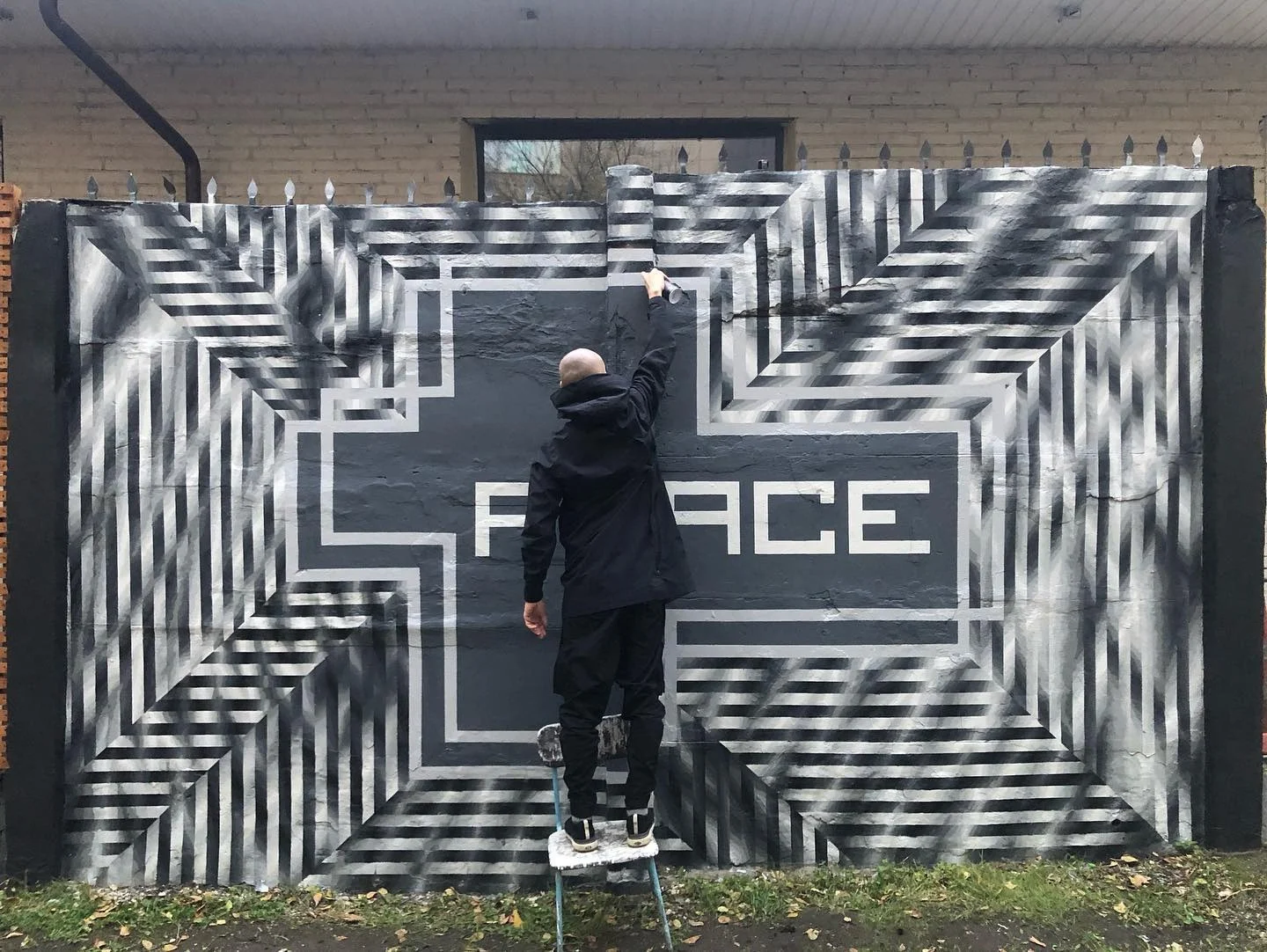 The artist painting an optical black-and-white mural on a concrete fence