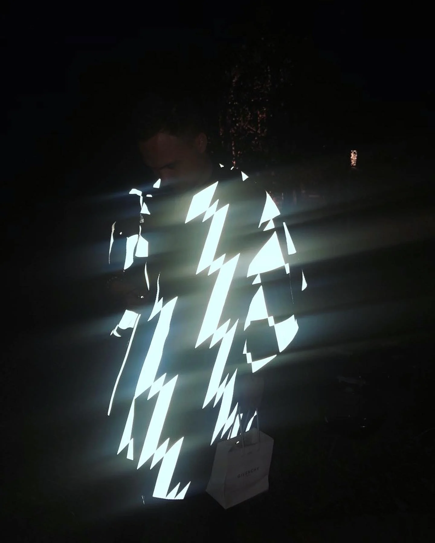 The raincoat at night, the reflective print glowing in a flash